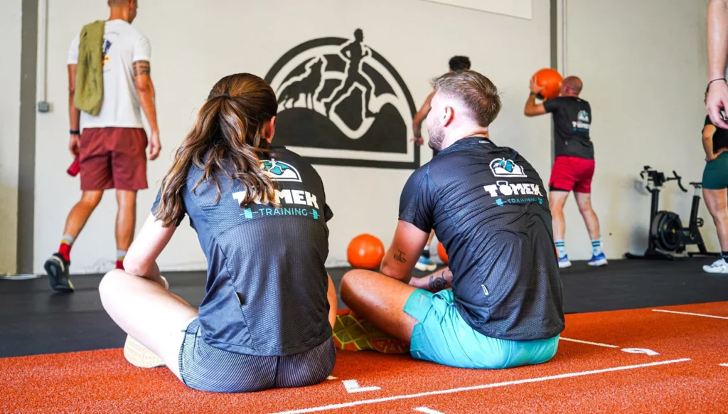 Deux adhérents en t-shirt Tomek Training assis côte à côte sur la piste, pendant que le groupe s'entraîne